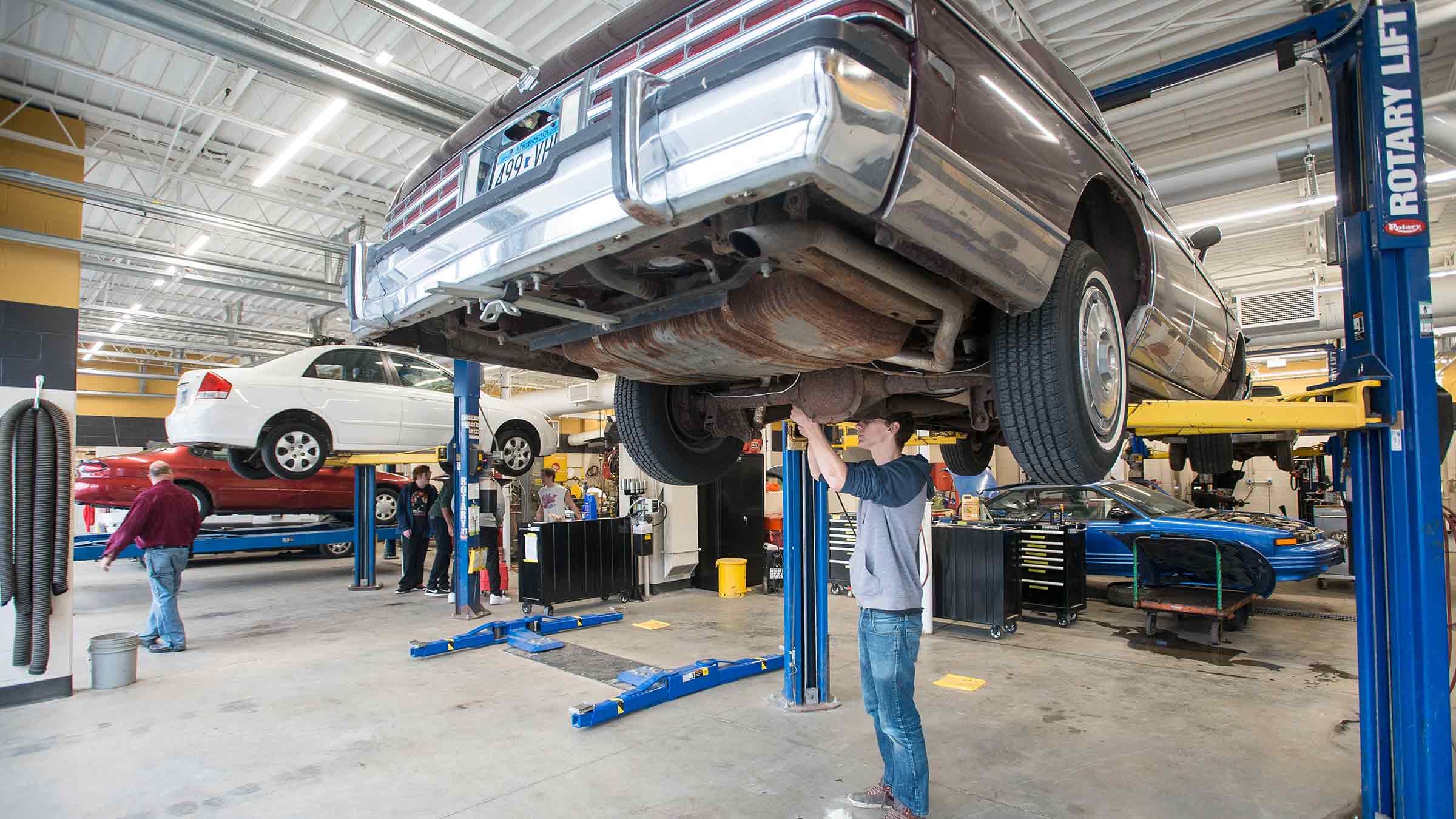 A high school student is fixing a part on a car as a part of Career Academies programming
