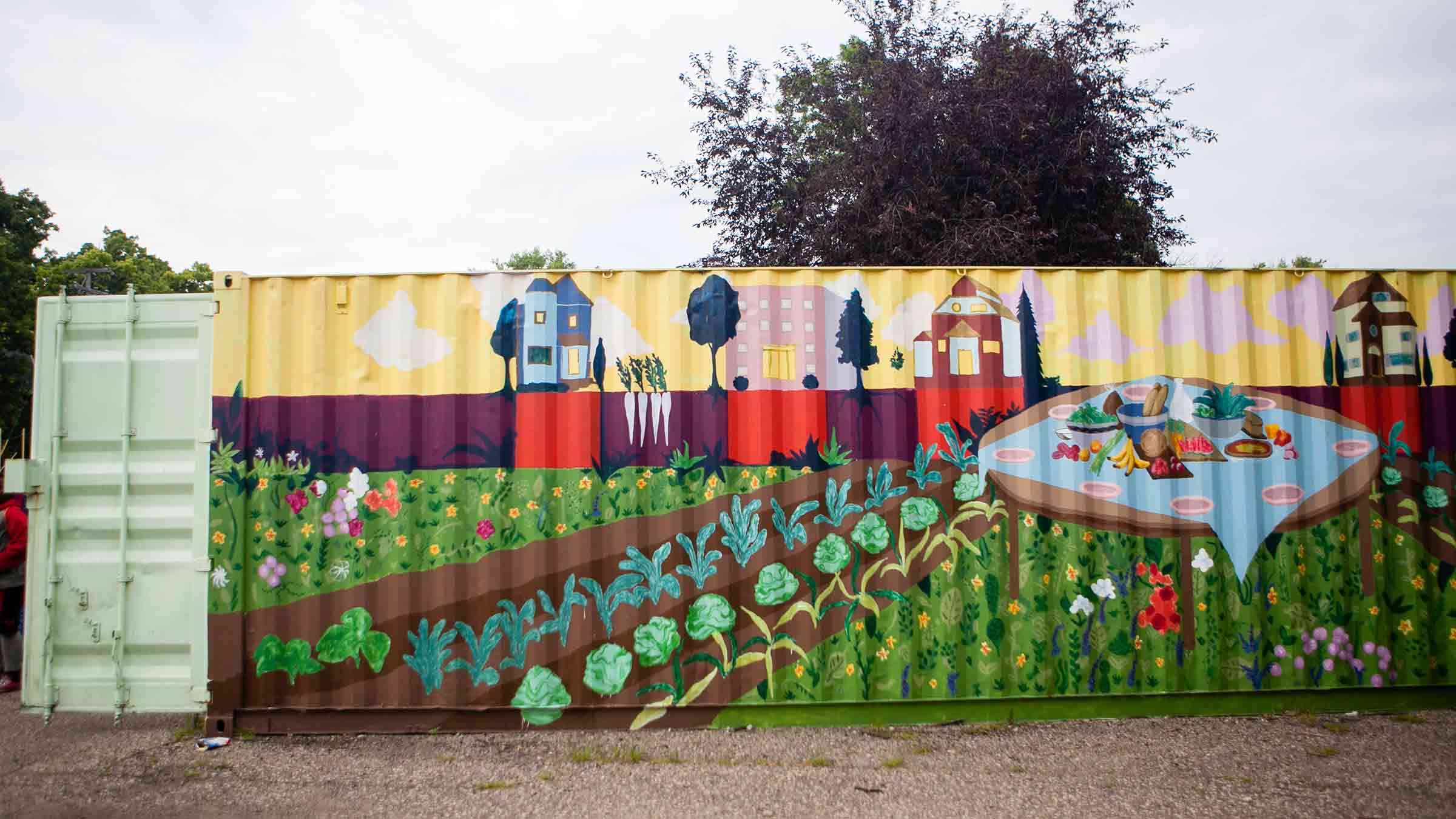 A mural shows a community garden with a table of fresh produce and houses in the background